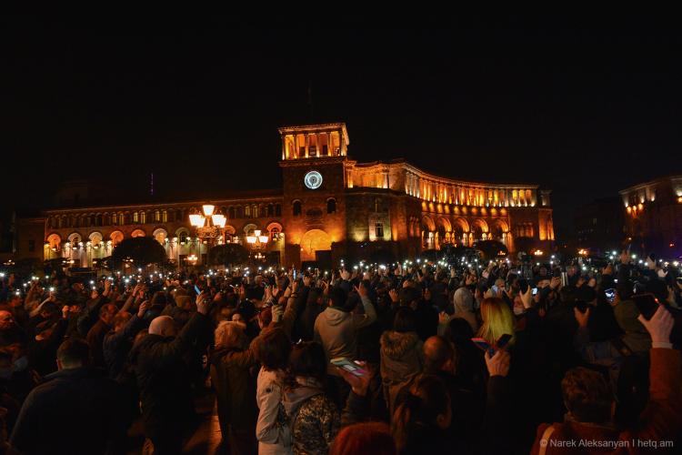 Crowd standing in the dark to protest in the capital. In the background some light building